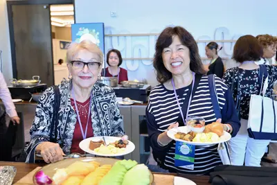 Two women smiling and holding breakfast plates at the AdventHealth Women's Health and Cancer Prevention Event