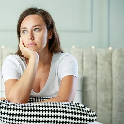 A woman sitting on her couch, looking thoughtful.