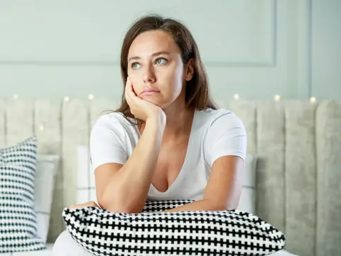 A woman sitting on her couch, looking thoughtful.