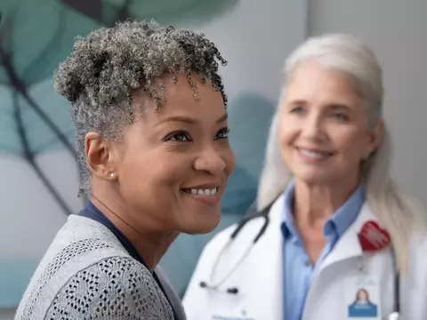 A smiling patient and a smiling doctor with a stethoscope around her neck.