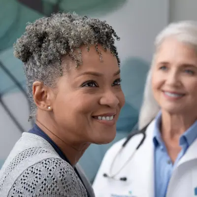 A smiling patient and a smiling doctor with a stethoscope around her neck.