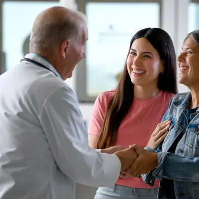 A doctor shakes hands with two smiling women, fostering a warm and positive atmosphere.