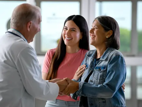 A doctor shakes hands with two smiling women, fostering a warm and positive atmosphere.
