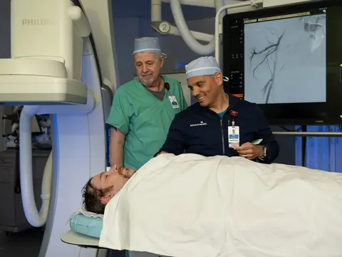 Two doctors in scrubs and a patient on a hospital bed in a medical room with a Philips monitor.