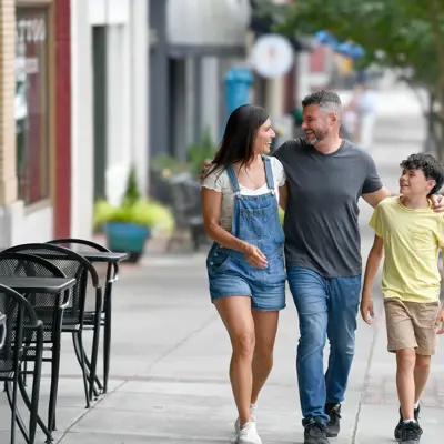 Family of three walking together on a downtown sidewalk, with a father in the middle embracing his teenage daughter and son as they smile and enjoy quality time together