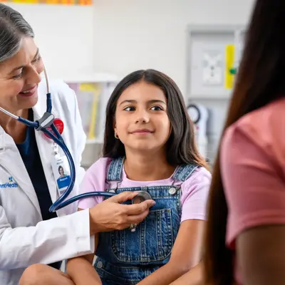 A doctor with a stethoscope listens to a young girl's heart, smiling warmly.