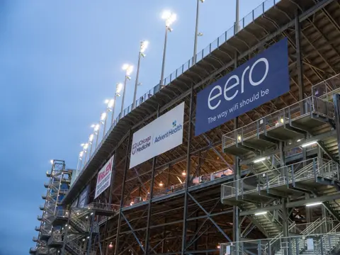 Exterior view of a stadium grandstand at dusk with illuminated sponsor signs, including UChicago Medicine, AdventHealth, and eero