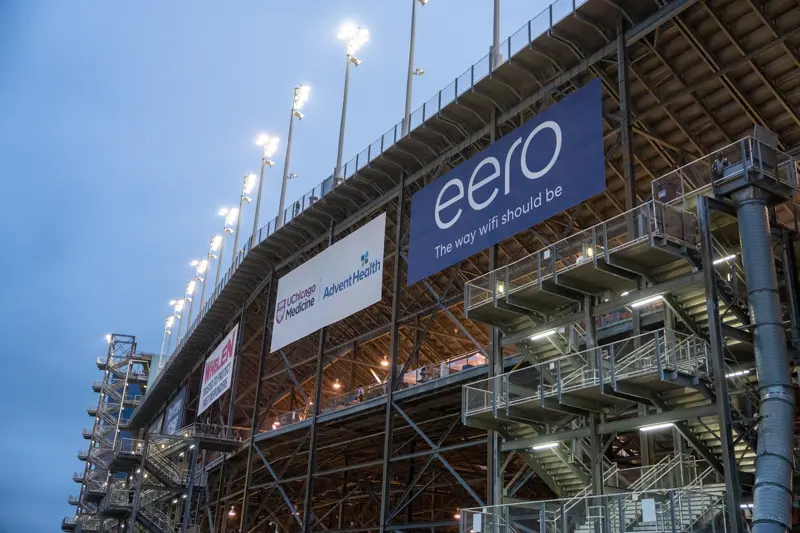 Exterior view of a stadium grandstand at dusk with illuminated sponsor signs, including UChicago Medicine, AdventHealth, and eero