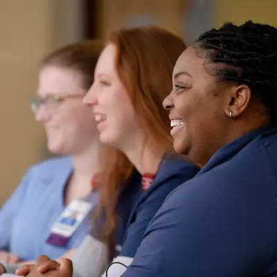 Three smiling women in blue scrubs sit together at a table, fostering a sense of community and support.