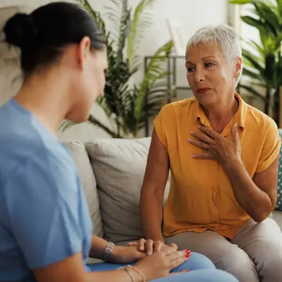 Older woman sitting on a couch speaking to a nurse.