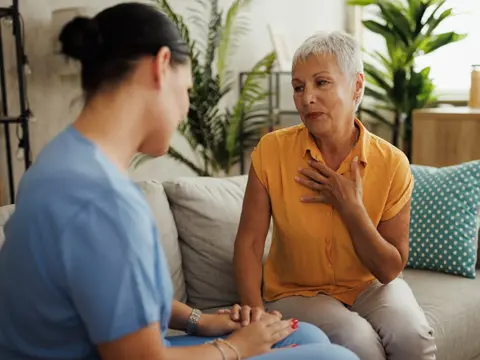 Older woman sitting on a couch speaking to a nurse.