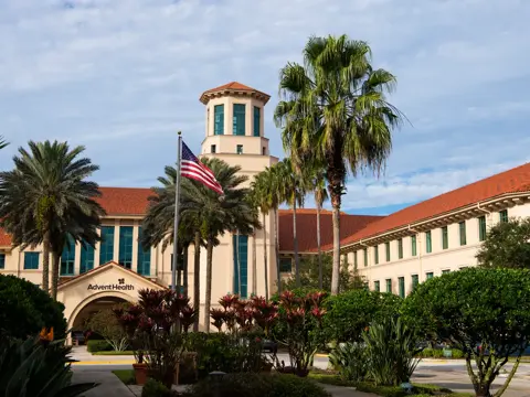 AdventHealth building with red roof, American flag, and lush greenery.