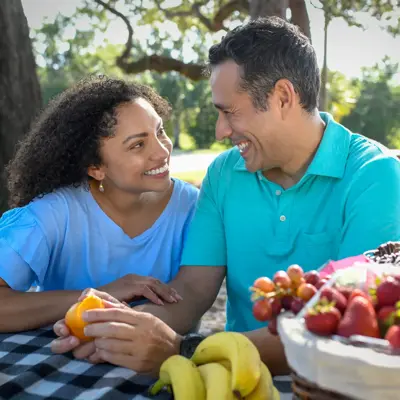 A smiling couple enjoys a picnic with fruit, showcasing a moment of joy and connection.