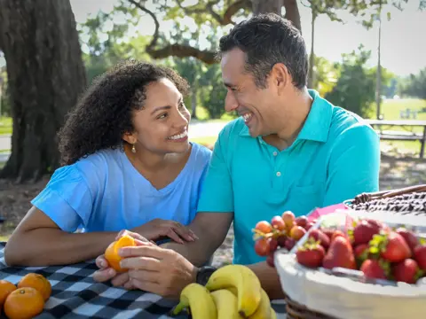 A smiling couple enjoys a picnic with fruit, showcasing a moment of joy and connection.