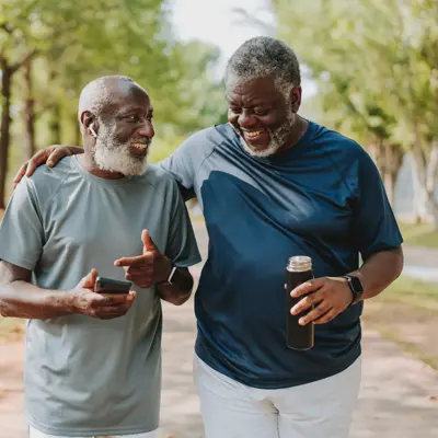 Two black senior friends walking together in public park.