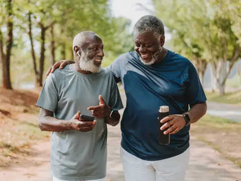 Two black senior friends walking together in public park.