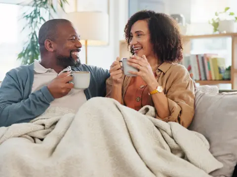Couple sipping from mugs under a blanket on their sofa