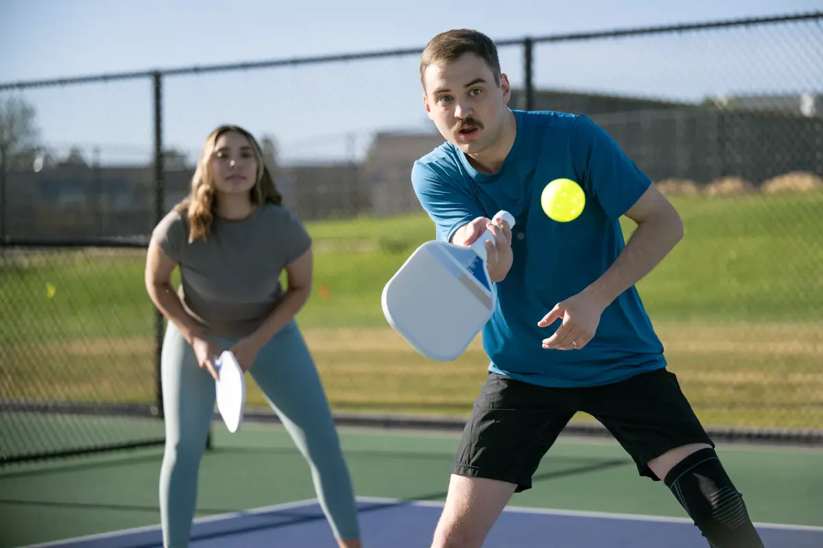A man and a woman playing pickleball on a court, with the man hitting the ball.