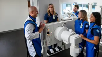 Imaging instructor demonstrating X-ray equipment to students wearing protective lead aprons in a clinical training lab