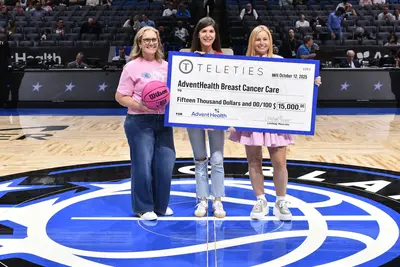 Three women holding up an oversized check at an Orlando Magic event.