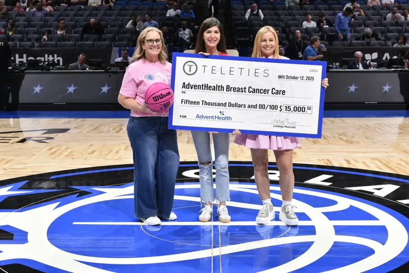 Three women holding up an oversized check at an Orlando Magic event.