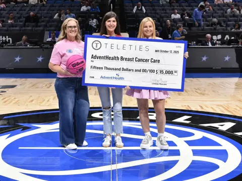 Three women holding up an oversized check at an Orlando Magic event.