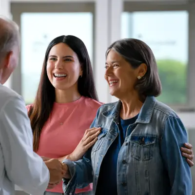 A smiling doctor shakes hands with two smiling women, fostering a warm and positive atmosphere.