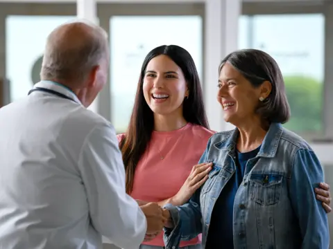 A smiling doctor shakes hands with two smiling women, fostering a warm and positive atmosphere.