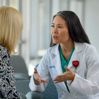 A doctor in a white coat and green shirt talks to a patient in a blue and white patterned shirt.