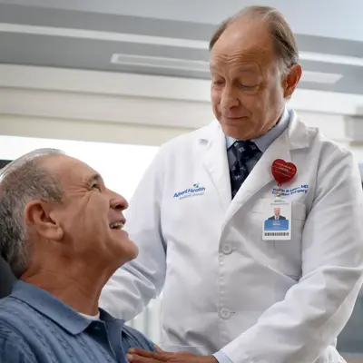 A smiling doctor in a white coat stands beside a seated patient, both smiling.