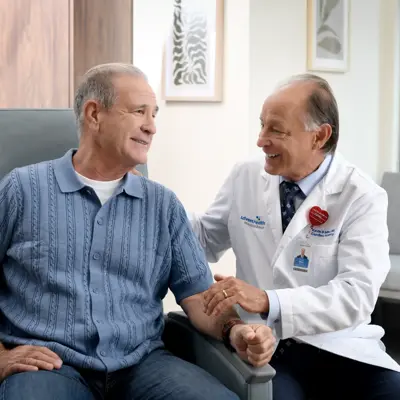 A smiling patient and a doctor in a medical office, holding hands and discussing health.