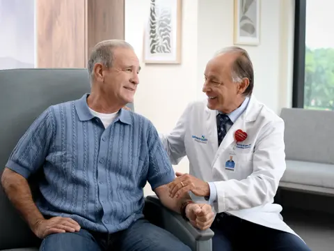 A smiling patient and a doctor in a medical office, holding hands and discussing health.