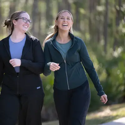 Two women walking and smiling in a forest, showcasing a sense of joy and companionship.