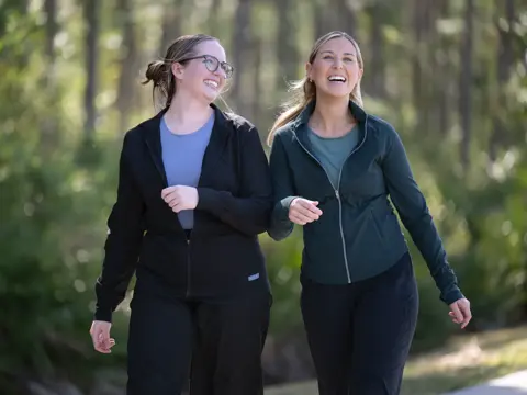 Two women walking and smiling in a forest, showcasing a sense of joy and companionship.