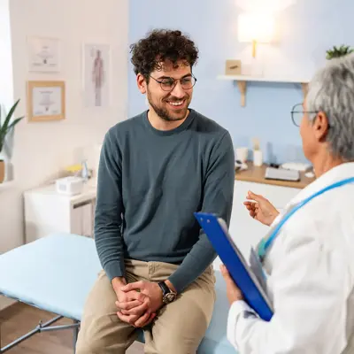 Male patient sitting on examination table while talking to doctor in a bright clinic room