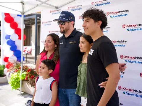 Group of five people pose for a photo with a race team member in front of a UChicago Medicine and AdventHealth event backdrop