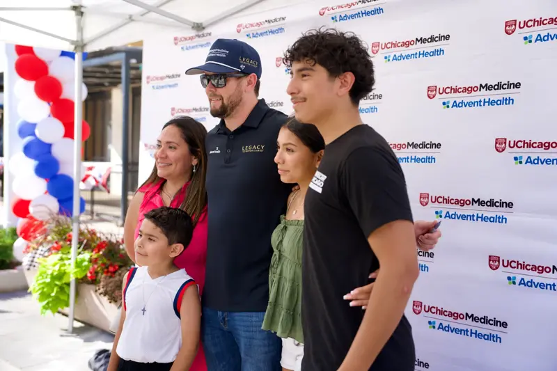 Group of five people pose for a photo with a race team member in front of a UChicago Medicine and AdventHealth event backdrop