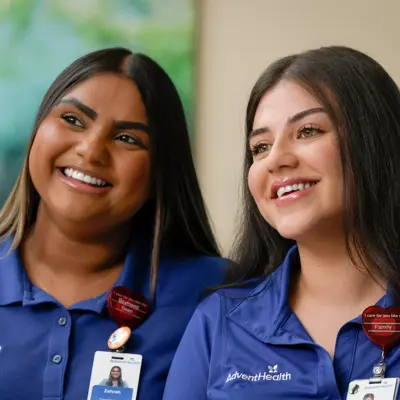 Two AdventHealth employees smiling and wearing blue uniforms with name tags.
