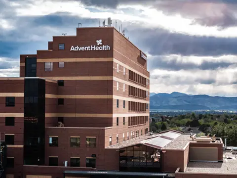 AdventHealth building with a modern design, set against a backdrop of mountains and cloudy sky.
