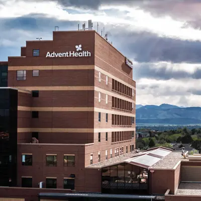 AdventHealth building with a modern design, set against a backdrop of mountains and cloudy sky.