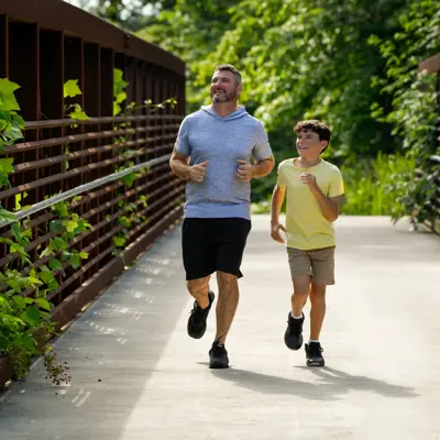Father and son jogging together on a wooden bridge surrounded by lush greenery