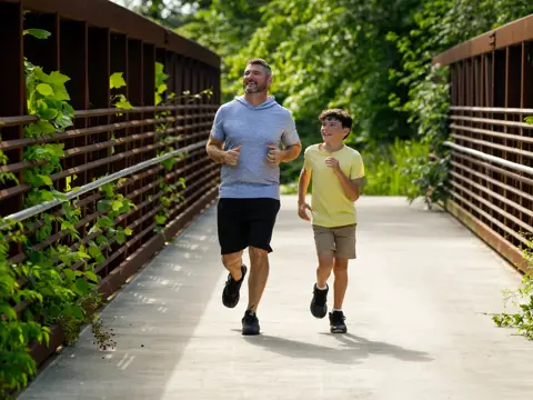 Father and son jogging together on a wooden bridge surrounded by lush greenery