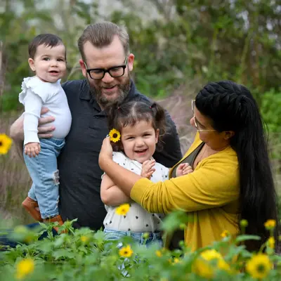 A family of four, consisting of a man, a woman, and two children, smiling in a field of flowers.