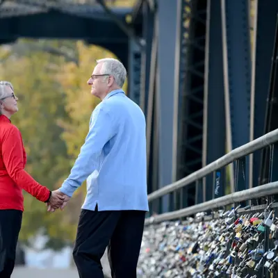 Elderly couple holding hands while walking on a bridge with padlocks.