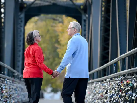 Elderly couple holding hands while walking on a bridge with padlocks.