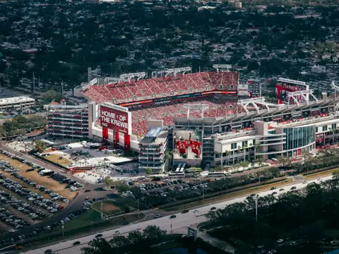 Aerial view of Raymond James Stadium filled with fans during a game, with Tampa city skyline visible in the background