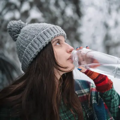 Woman drinking water in the winter woods.