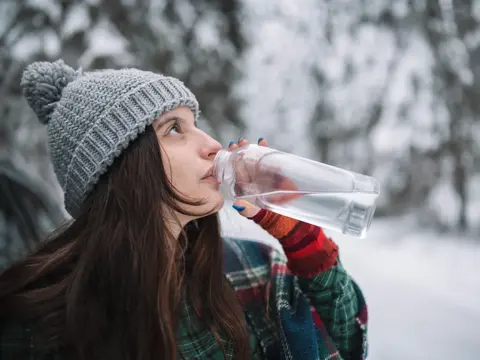 Woman drinking water in the winter woods.