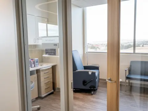 Modern private infusion suite with reclining treatment chairs, medical equipment, and large windows overlooking a landscape