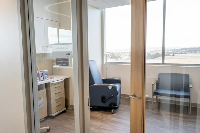 Modern private infusion suite with reclining treatment chairs, medical equipment, and large windows overlooking a landscape